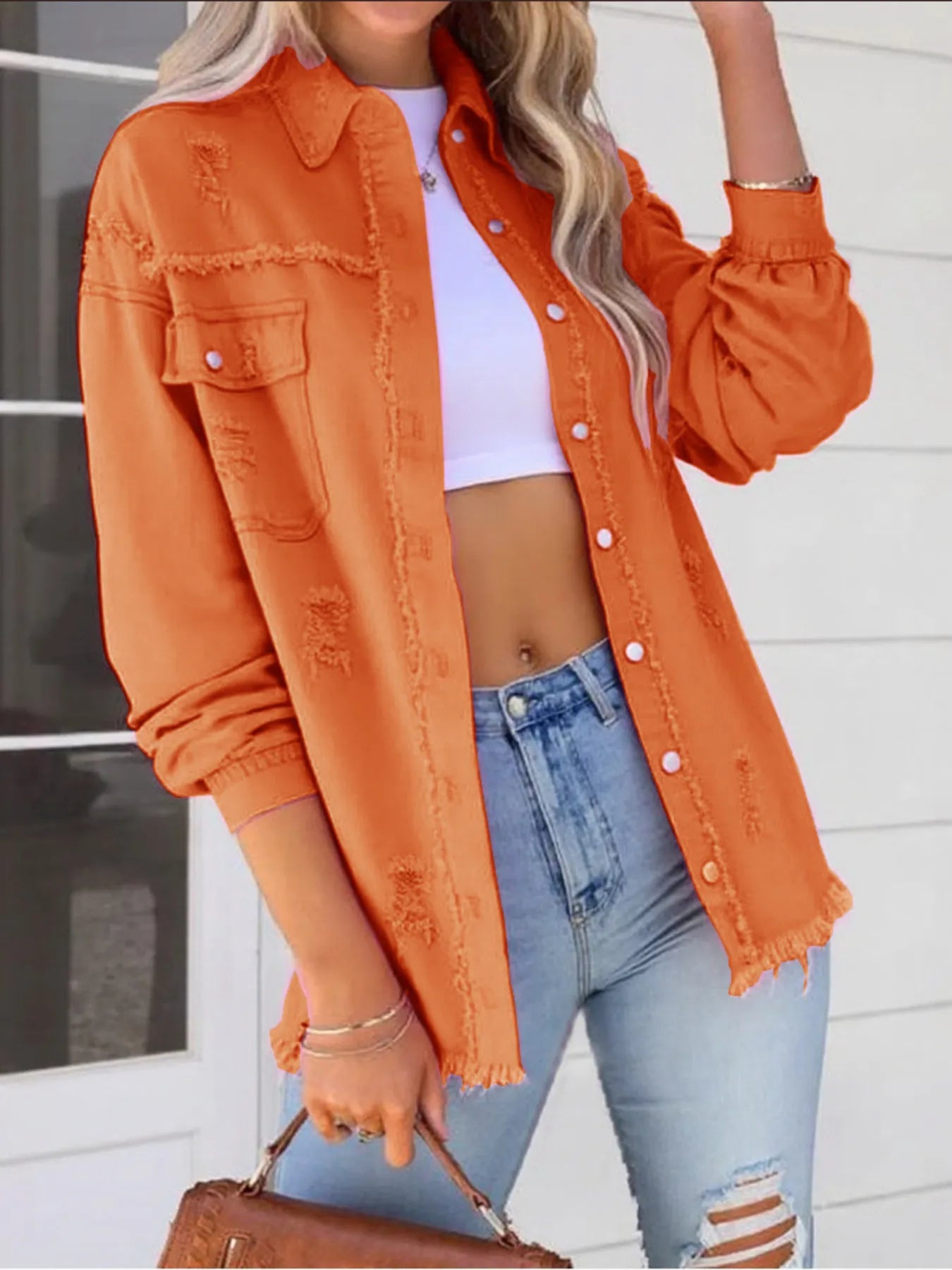 Trendy oversized distressed denim jacket with frayed edges and buttoned pockets, styled in orange color, paired with a cropped white top and high-waisted jeans for a casual chic look.