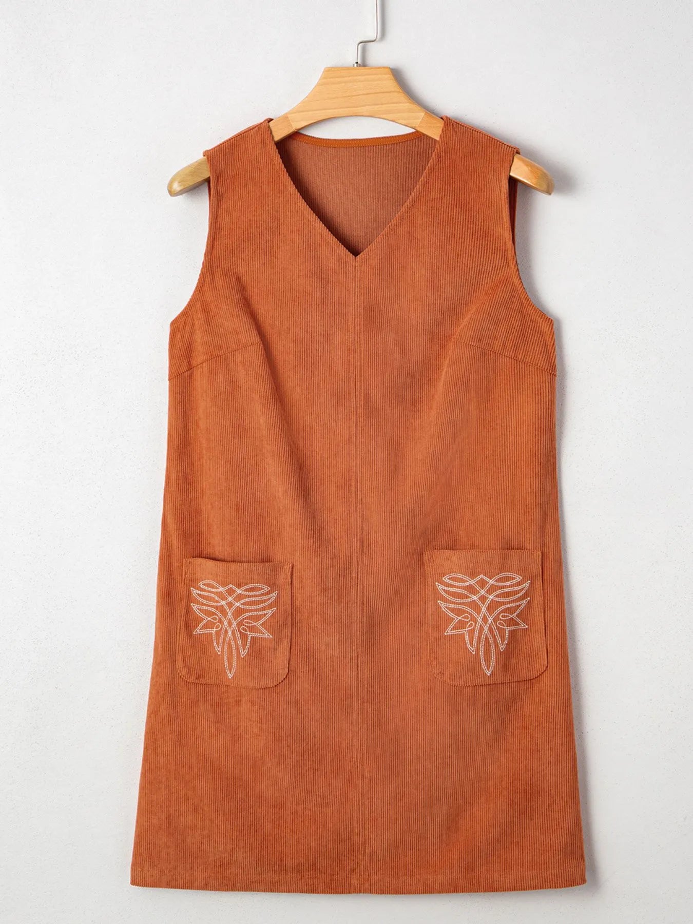 Front view of the Corduroy Western Mini Dress With Embroidered Patch Pocket displayed on a hanger, demonstrating its unique corduroy texture and embroidered pockets.