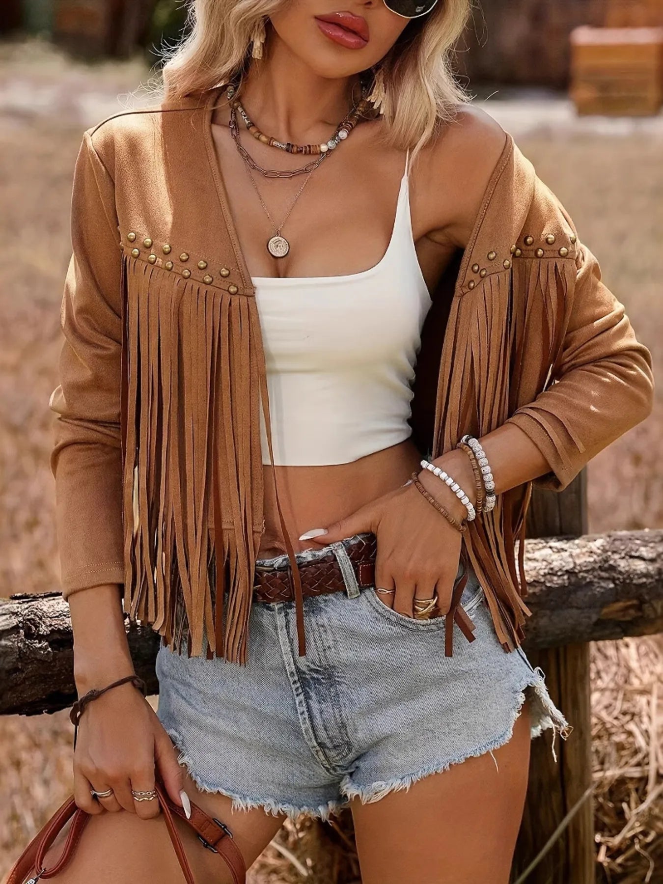 Close-up view of the Trendy Fringe Studded Open Front Jacket, highlighting the fringe and studded design, worn with a crop top and denim shorts, set against a natural background.