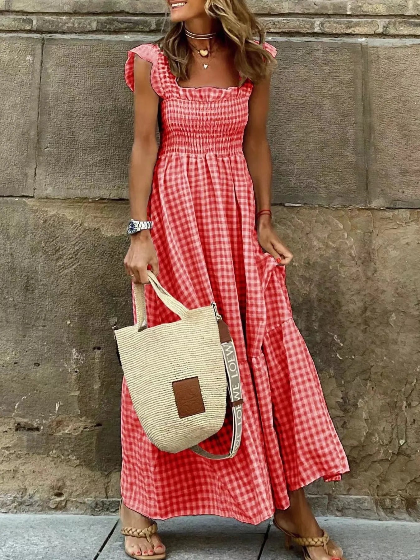Fashionable woman in a Gingham Maxi Dress with Ruffle Straps, Smocked Bodice & Tiered Design in red and white check, holding a stylish straw bag.