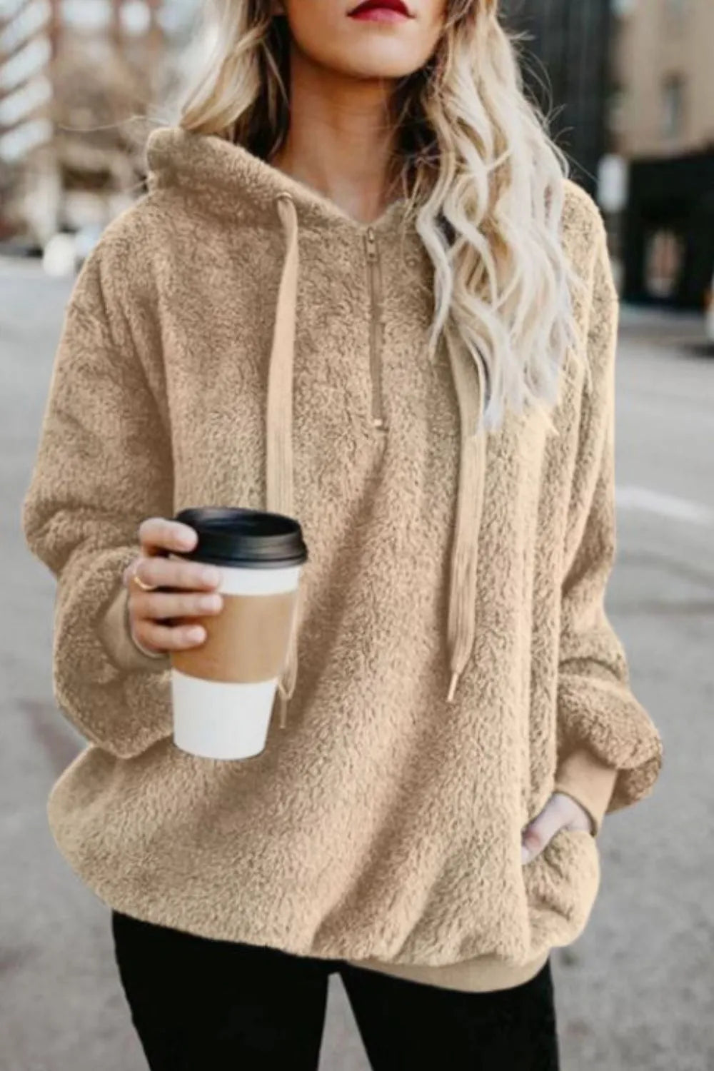 Fashionable woman wearing the Cozy Full Size Teddy Hoodie with Quarter-Zip and Drawstring in beige, holding a coffee cup in an outdoor setting.