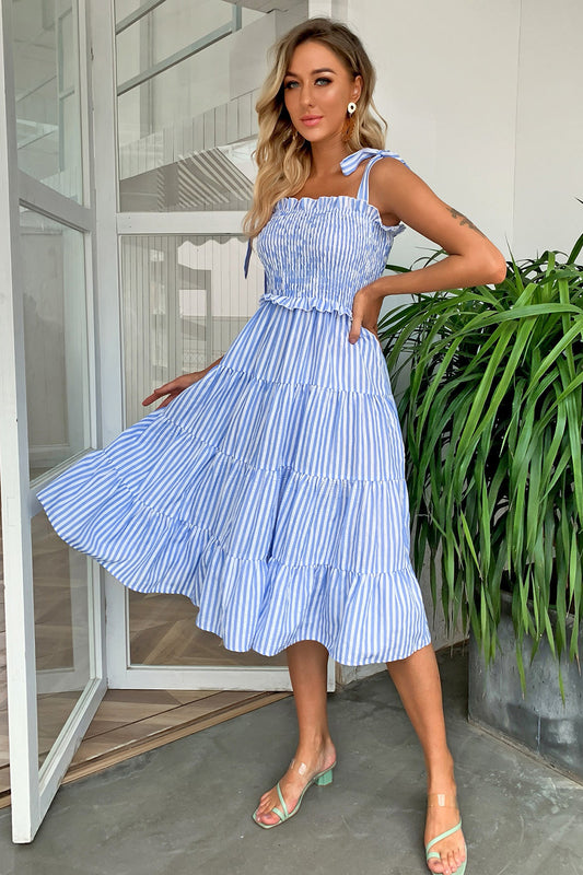 Trendy Striped Tie-Shoulder Tiered Dress with Smocked Ruffled Details, featuring a beautiful light blue and white striped pattern, worn by a model in a stylish indoor setting.