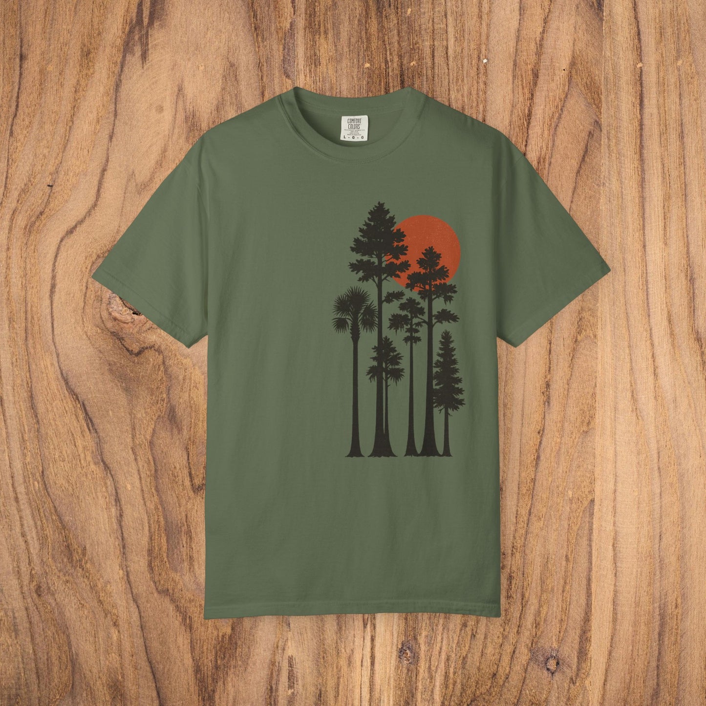 Sunset Trees Unisex T-Shirt in olive green, featuring a comfortable fit and made from 100% cotton, showcased on a rustic wood surface.