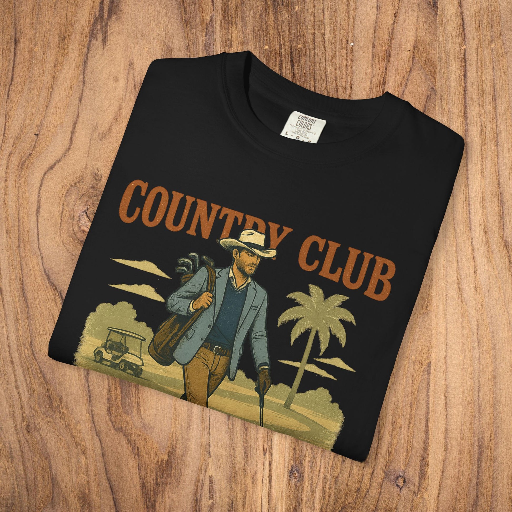Country Club Cowboy Graphic Tee in black, laid flat on wooden surface, emphasizing its durable cotton fabric and eye-catching graphic.
