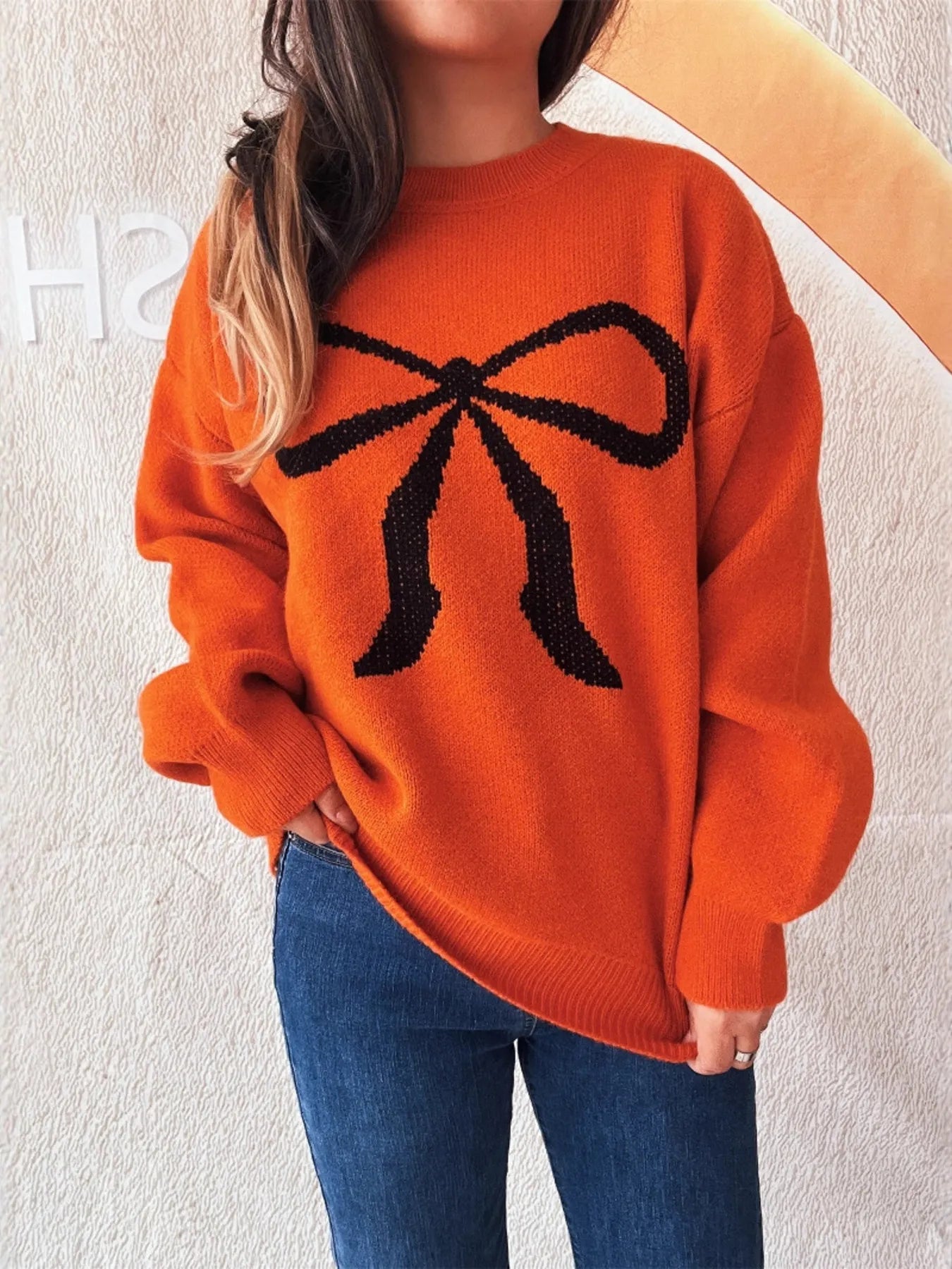 Casual long sleeve sweater featuring a stylish bow pattern, perfect for effortless everyday wear. Model wearing in vibrant orange.