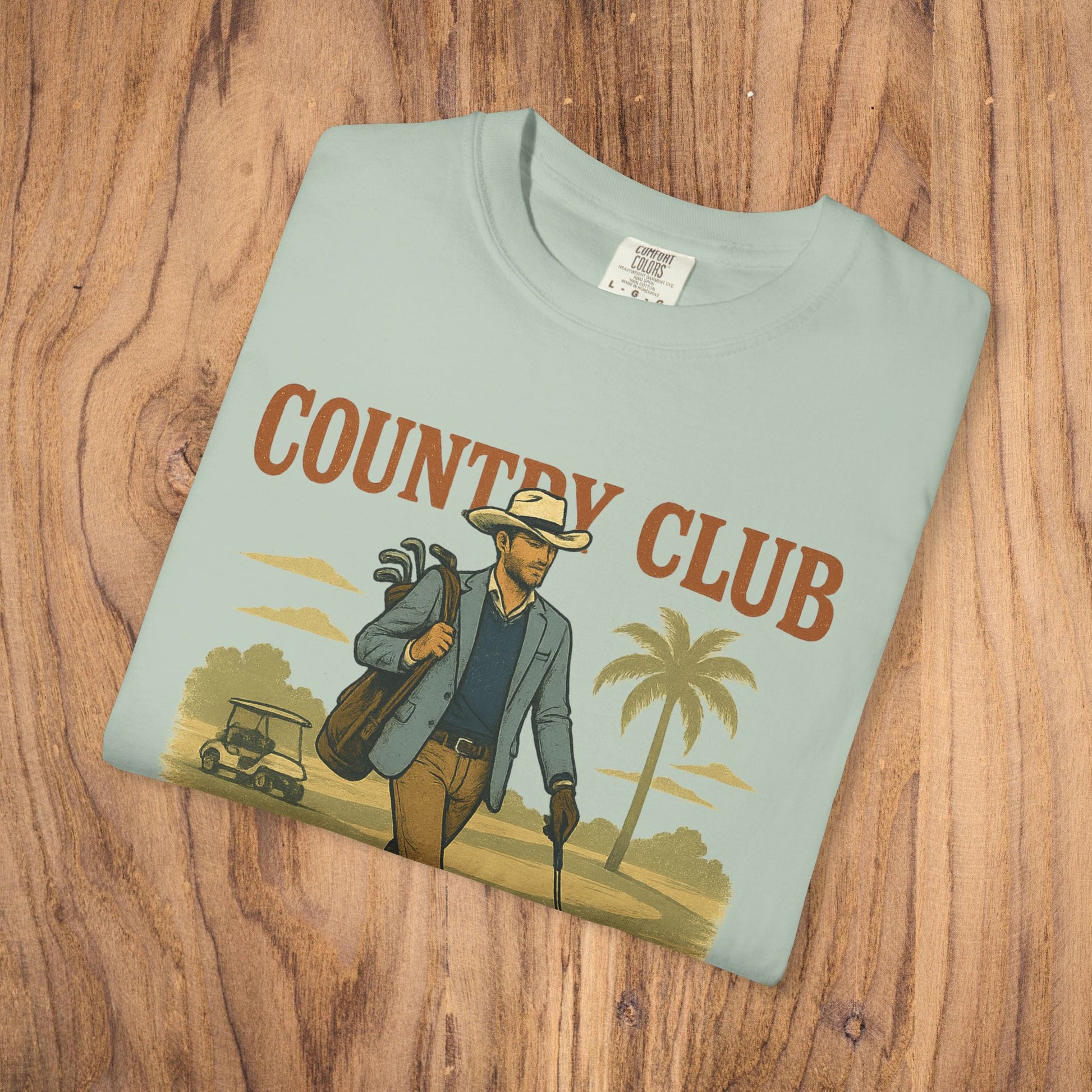 Country Club Cowboy Graphic Tee displayed on a wooden surface, showcasing a stylish design with a cowboy theme, perfect for casual wear.