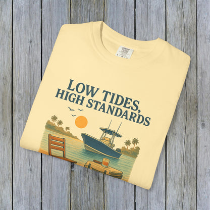 Garment-Dyed Low Tides High Standards T-Shirt folded on a textured wooden background, highlighting its soft fabric and colorful beach-themed graphic.