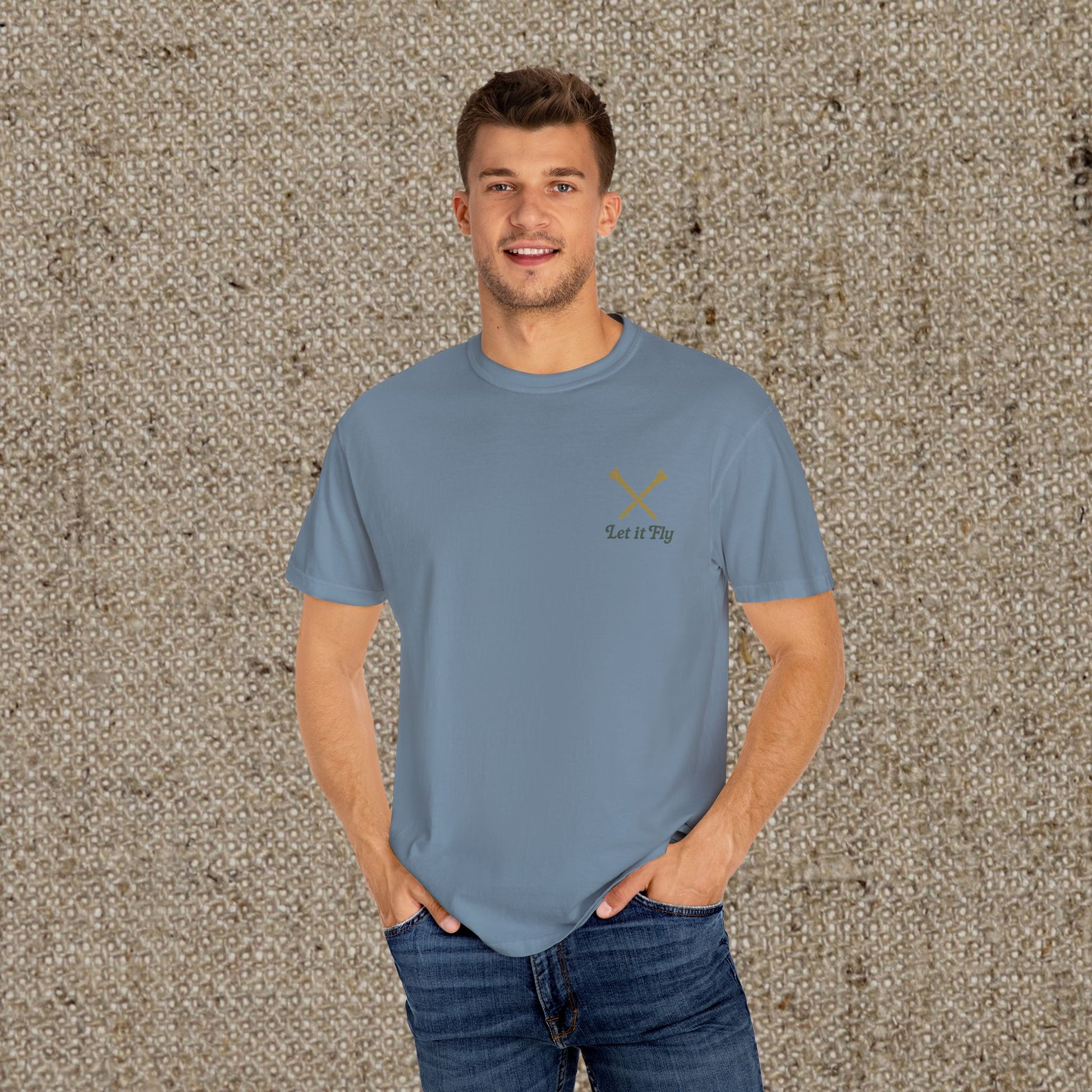 Model wearing the stylish Tee It High Let It Fly Graphic Tee in blue, featuring crossed clubs and 'Let It Fly' text, perfect for golf lovers.