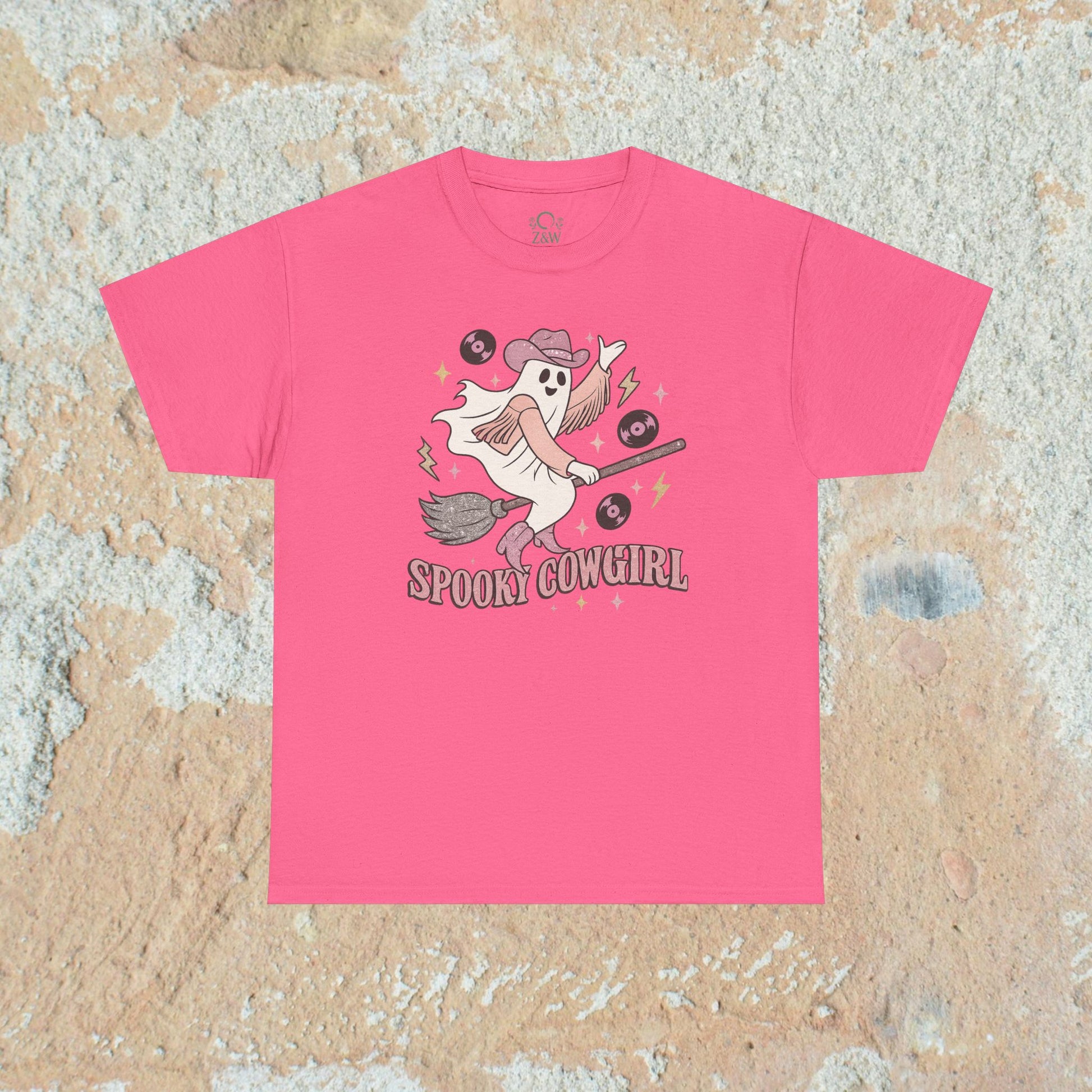 Bright pink Spooky Cowgirl graphic tee featuring a lively ghost with a broomstick and records, perfect for adding a playful touch to any Halloween outfit. Sizes S to 5XL.