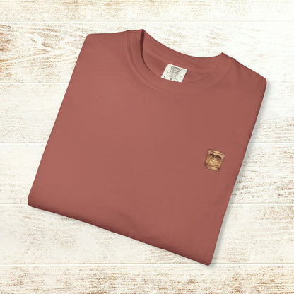 Folded Rodeo On The Rocks Tee in a warm hue, with a logo of a drink glass, emphasizing its soft, durable fabric and unique garment-dyed style.