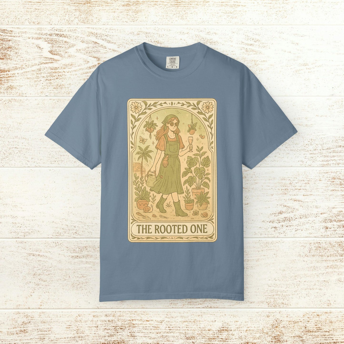 Rooted One Tarot Tee in light blue, featuring an enchanting design of a character alongside greenery. Ethically sourced cotton ensures comfort and sustainability.