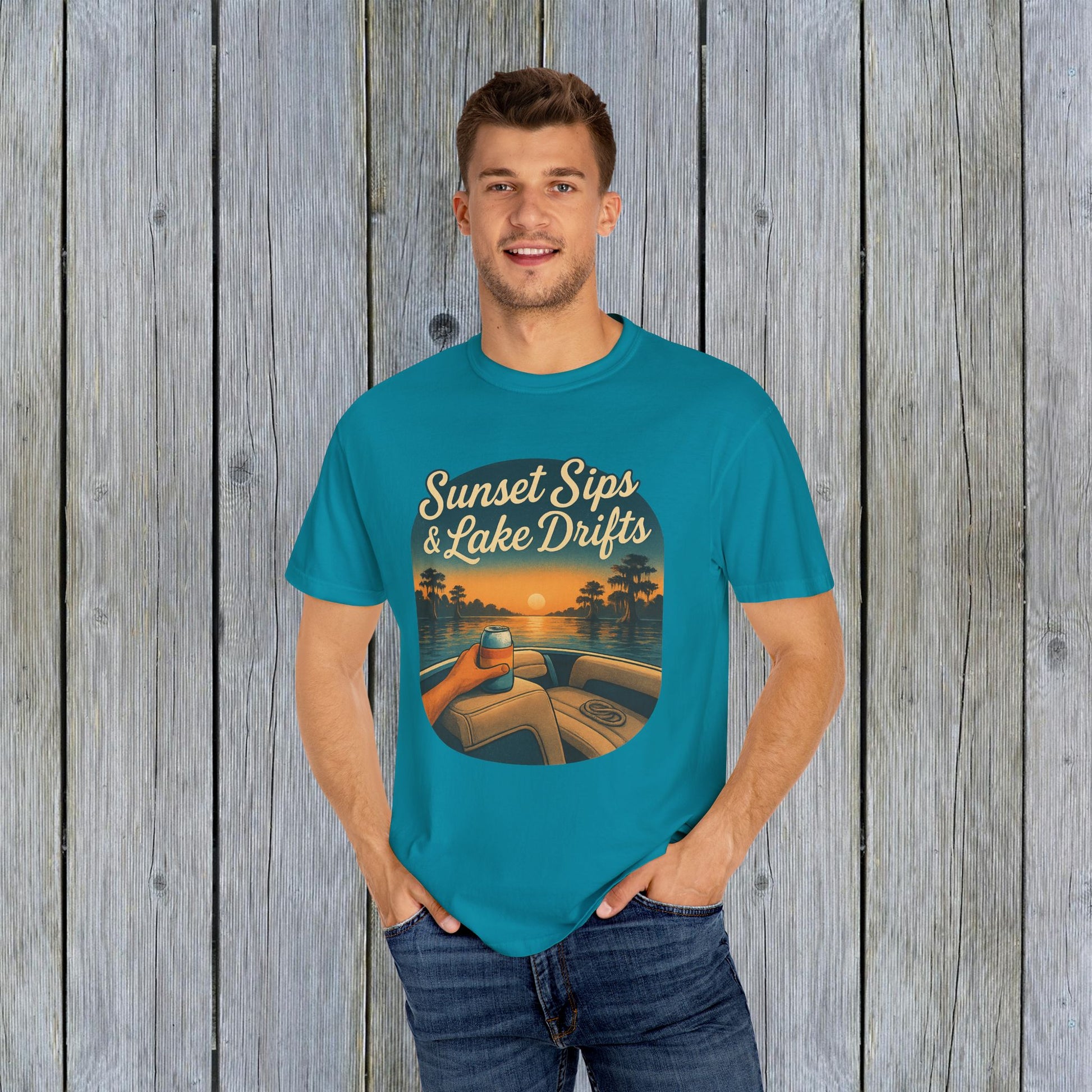 Model wearing the Lake Drifts T-Shirt in vibrant turquoise, featuring the design 'Sunset Sips & Lake Drifts' against a wood backdrop.