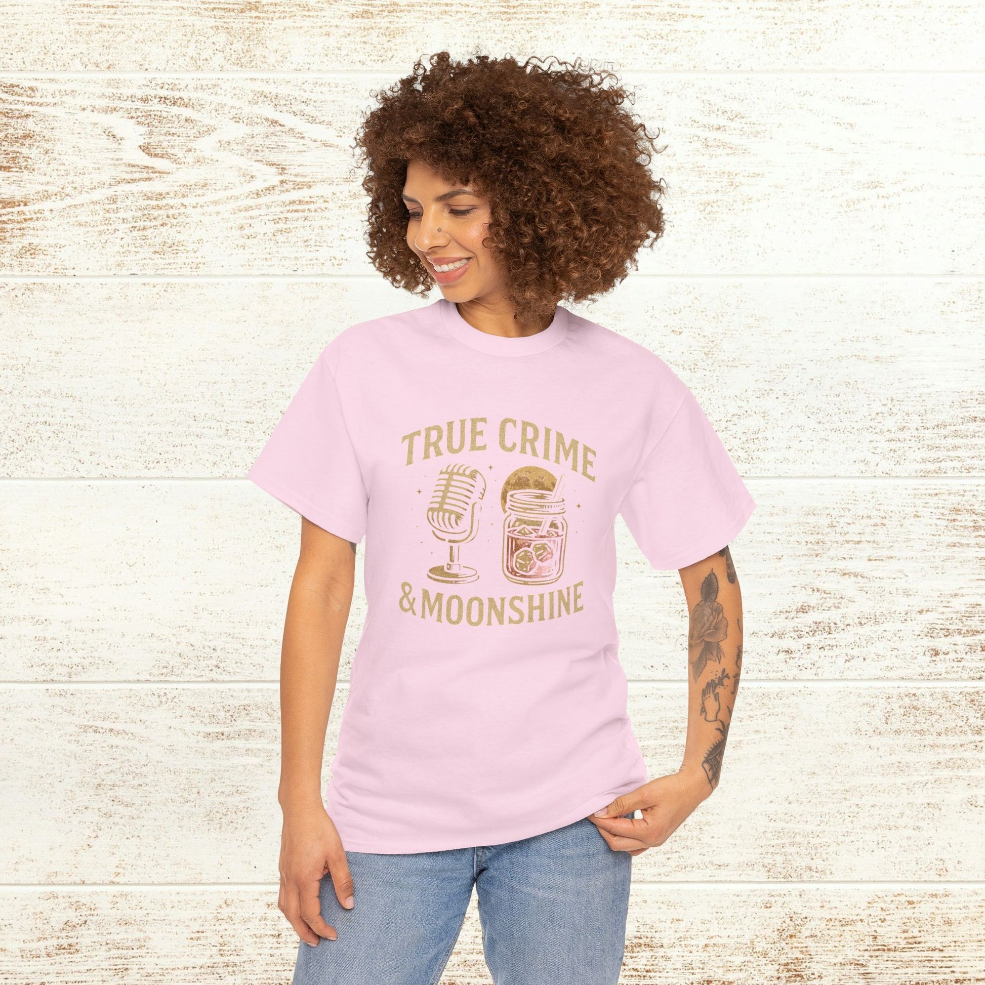 Model wearing True Crime & Moonshine Unisex Graphic Tee in soft pink against a rustic wooden backdrop, highlighting its stylish and casual vibe for true crime enthusiasts.