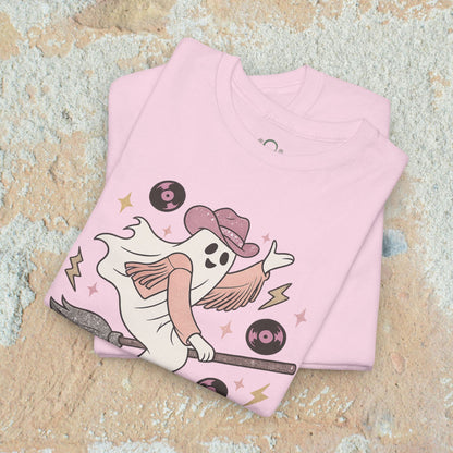 Spooky Cowgirl Graphic Tee with a fun ghost design in a stack of pink shirts, featuring a cowboy hat and broom, perfect for Halloween enthusiasts looking for soft, eco-friendly fashion.