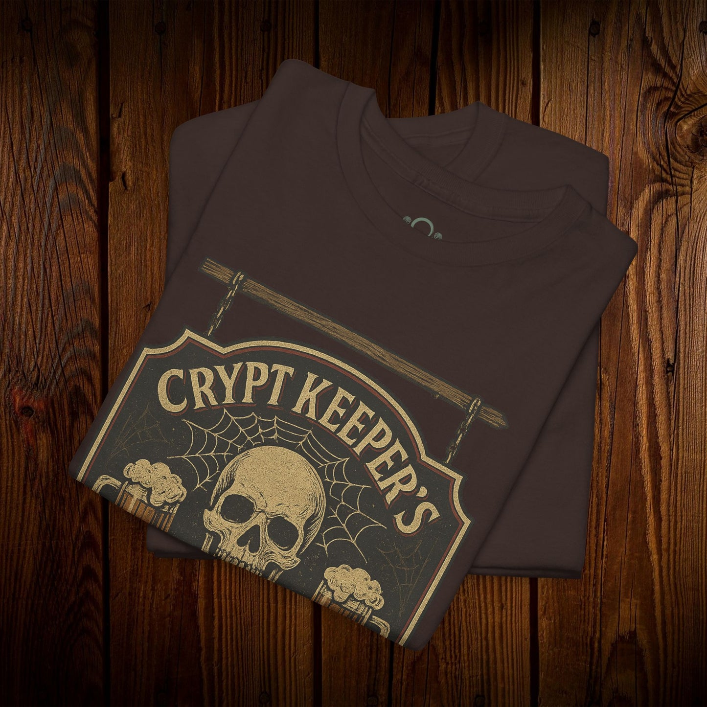 Crypt Keeper's Pub Tee in a rich brown color showcasing a unique skull graphic with a spiderweb, ideal for Halloween festivities and everyday casual attire. Crafted from 100% cotton for lasting quality.