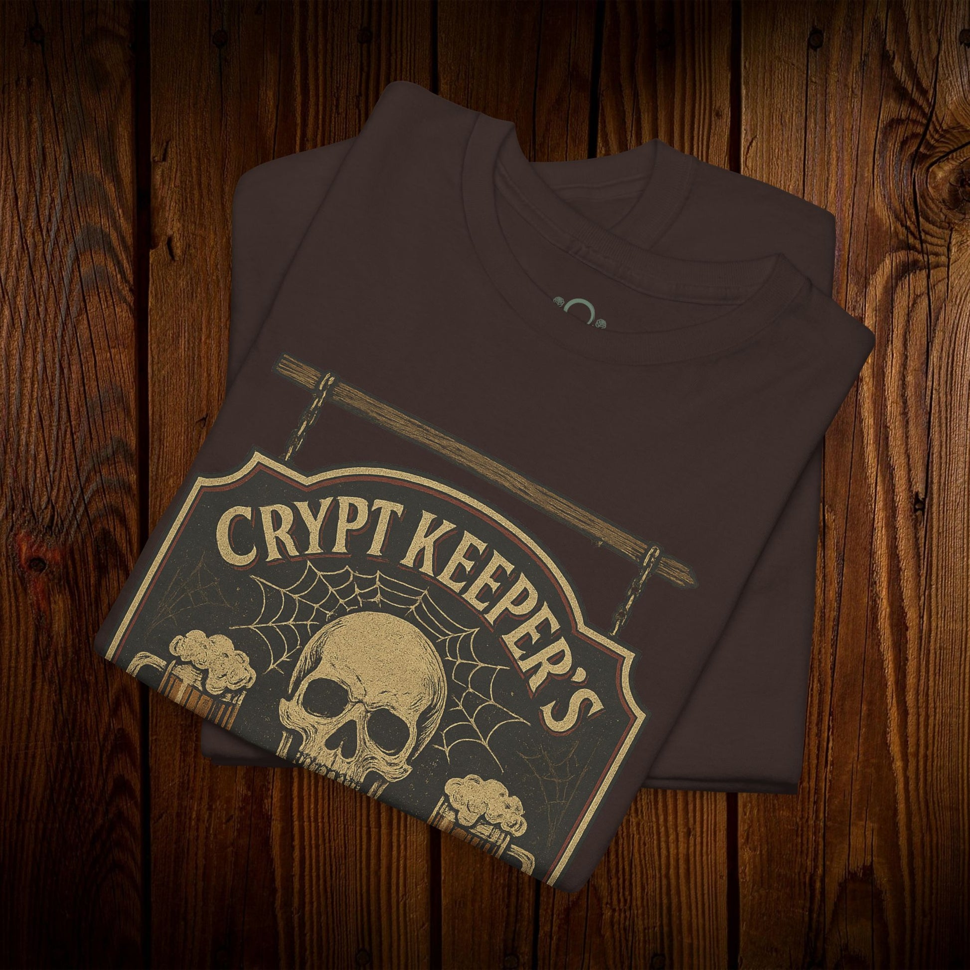 Crypt Keeper's Pub Tee in a rich brown color showcasing a unique skull graphic with a spiderweb, ideal for Halloween festivities and everyday casual attire. Crafted from 100% cotton for lasting quality.