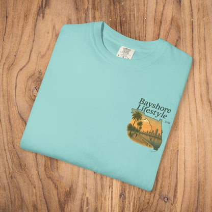Bayshore Lifestyle Tee displayed in light blue color, featuring a beach sunset design, made from 100% cotton.