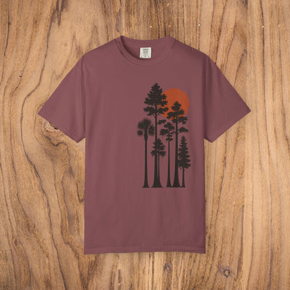 Sunset Trees Unisex T-Shirt in maroon, crafted from high-quality 100% cotton with a stylish garment-dyed texture, displayed on a natural wood background.