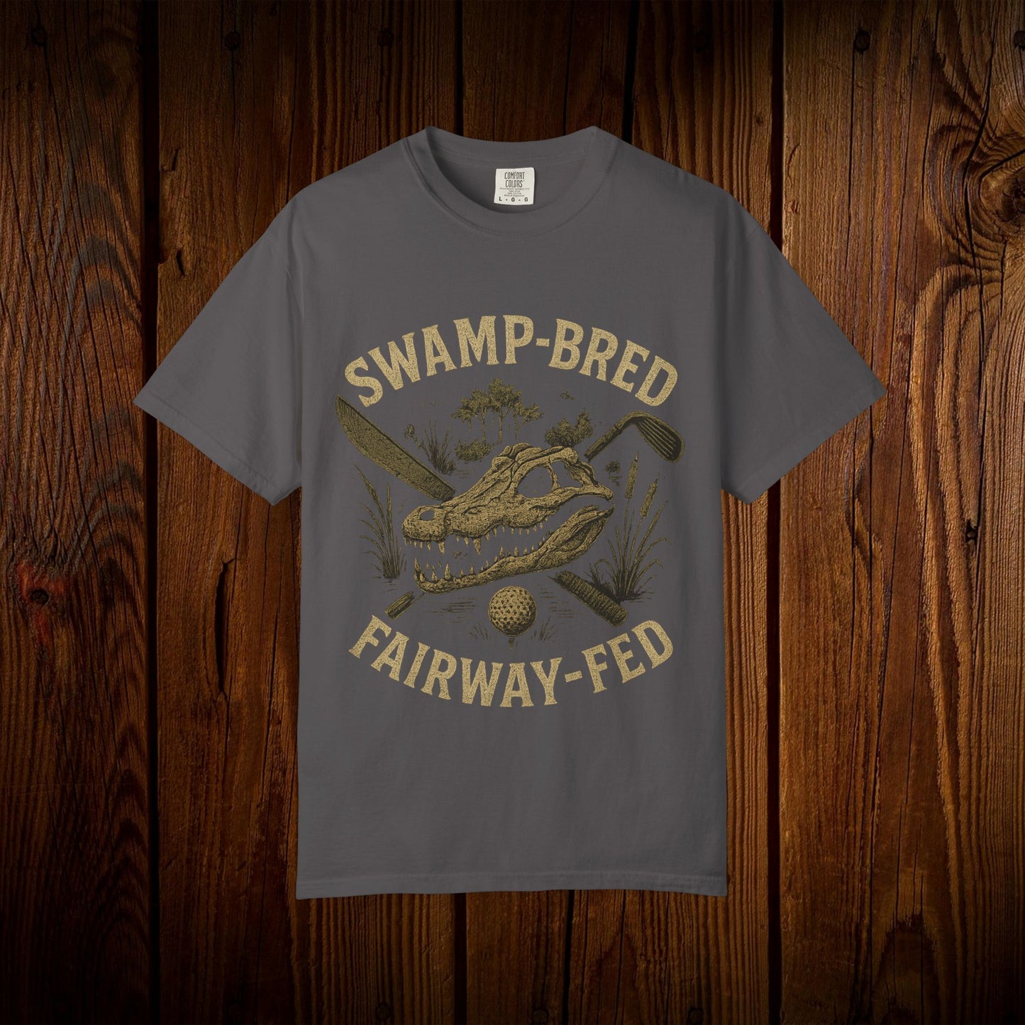 Unisex Swamp-Bred Fairway-Fed Tee in dark gray, showcasing a unique printed design featuring an alligator skull and golf elements on a rustic wooden background.