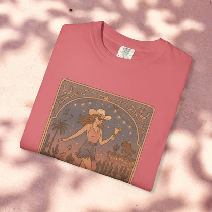 Line Dancer Tarot Tee crafted from soft cotton, shown in vibrant raspberry pink. This unique design features a lively woman in a cowboy hat dancing against a backdrop of desert plants and stars, available in sizes S-4XL and ethically made.