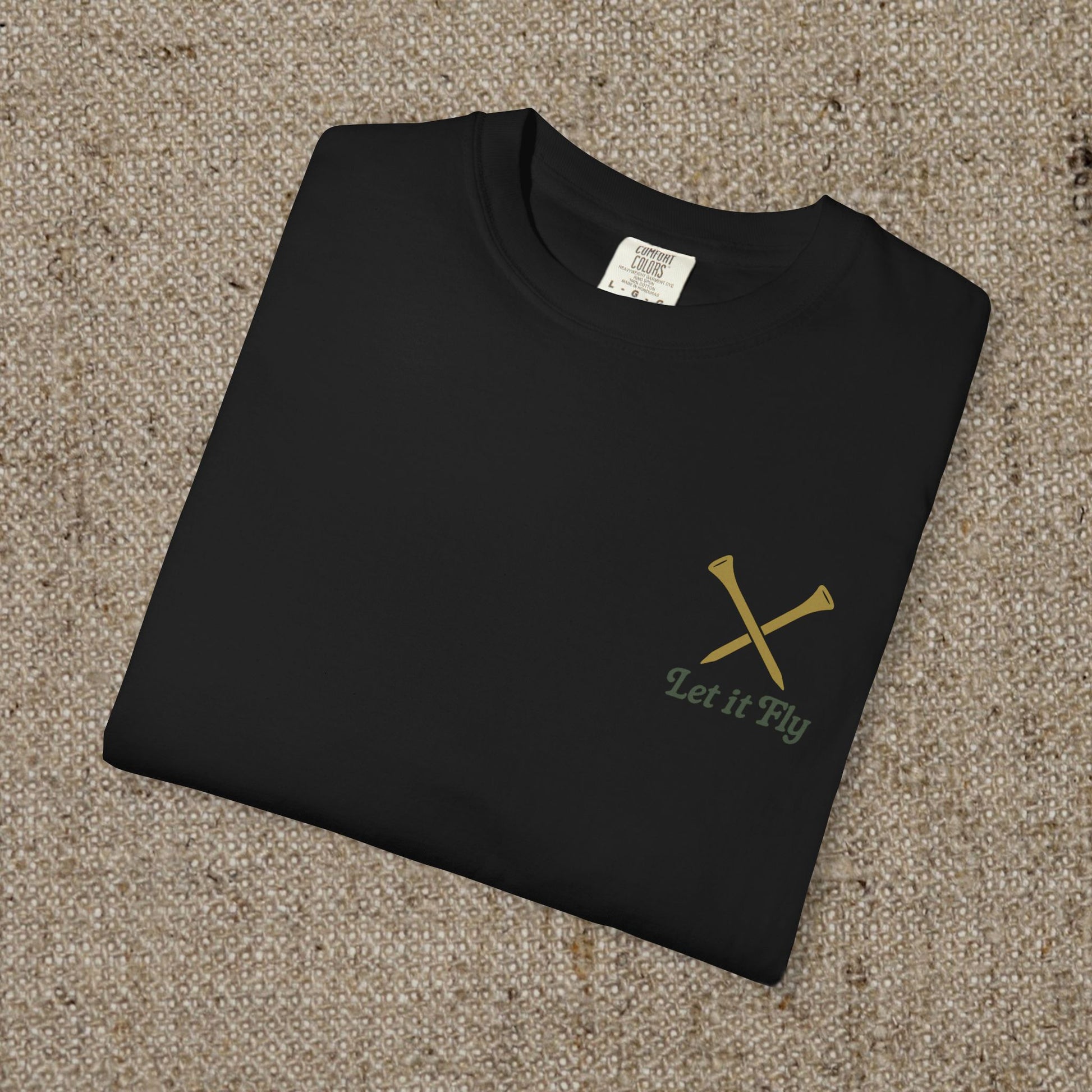 Folded Tee It High Let It Fly Graphic Tee showcasing a minimalist design with crossed golf clubs and the phrase 'Let it Fly', ideal for casual wear.