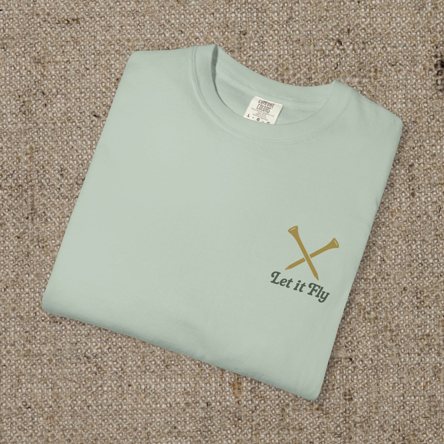 Folded Tee It High Let It Fly Graphic Tee in light green, showcasing the stylish design with 'Let It Fly' text and crossed golf clubs on the chest.