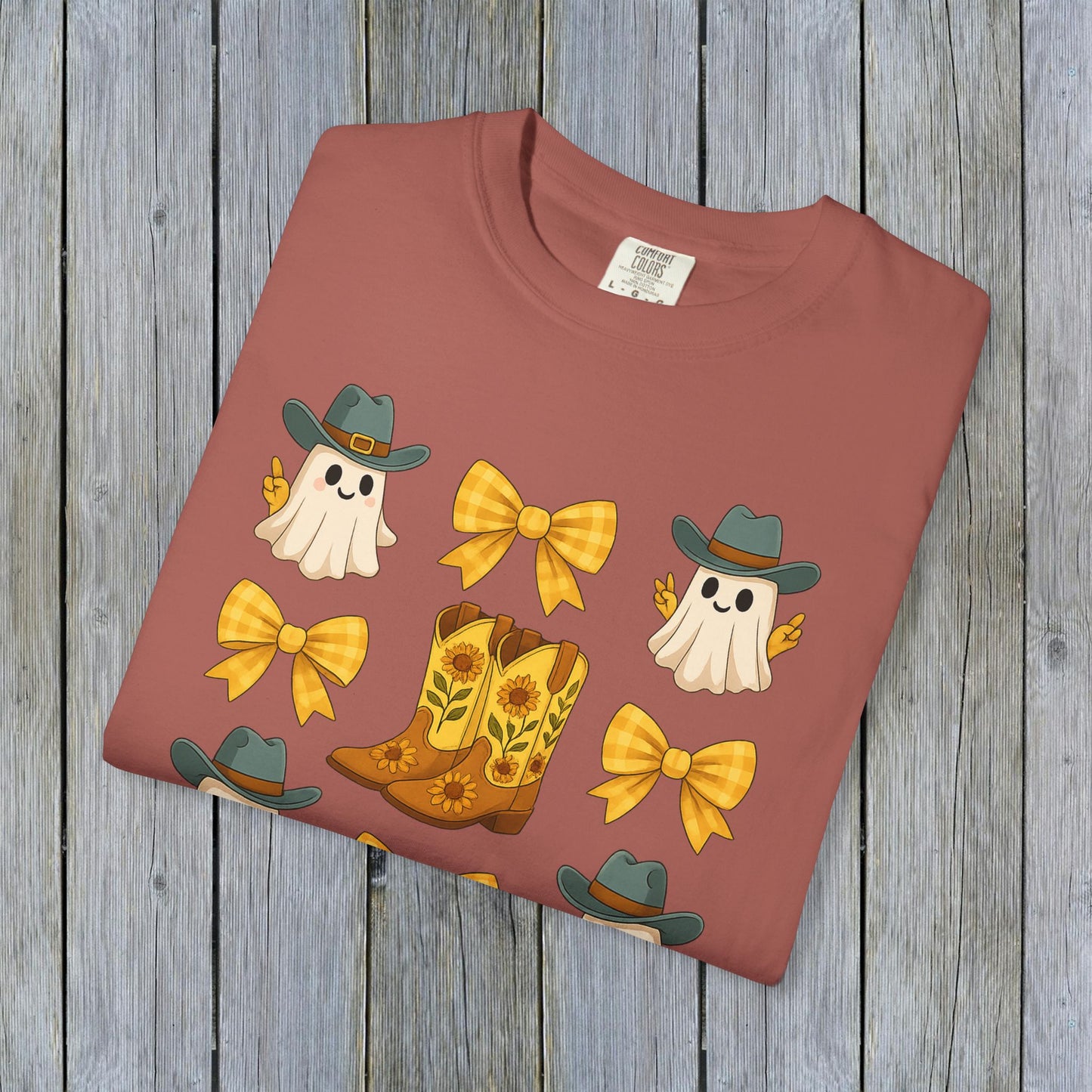Flat lay of Cute Halloween T-Shirt showcasing a playful graphic of ghosts, cowboy boots, and bows on a warm background, highlighting unisex fall fashion and eco-friendly fabric material.