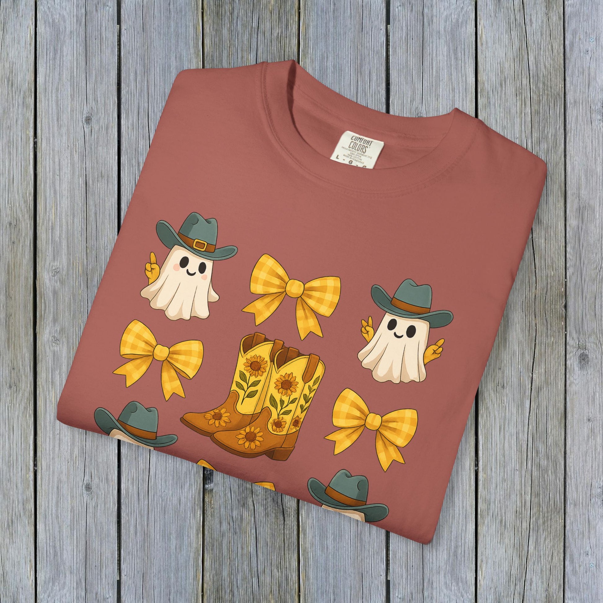 Flat lay of Cute Halloween T-Shirt showcasing a playful graphic of ghosts, cowboy boots, and bows on a warm background, highlighting unisex fall fashion and eco-friendly fabric material.