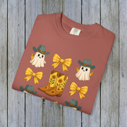 Flat lay of Cute Halloween T-Shirt showcasing a playful graphic of ghosts, cowboy boots, and bows on a warm background, highlighting unisex fall fashion and eco-friendly fabric material.