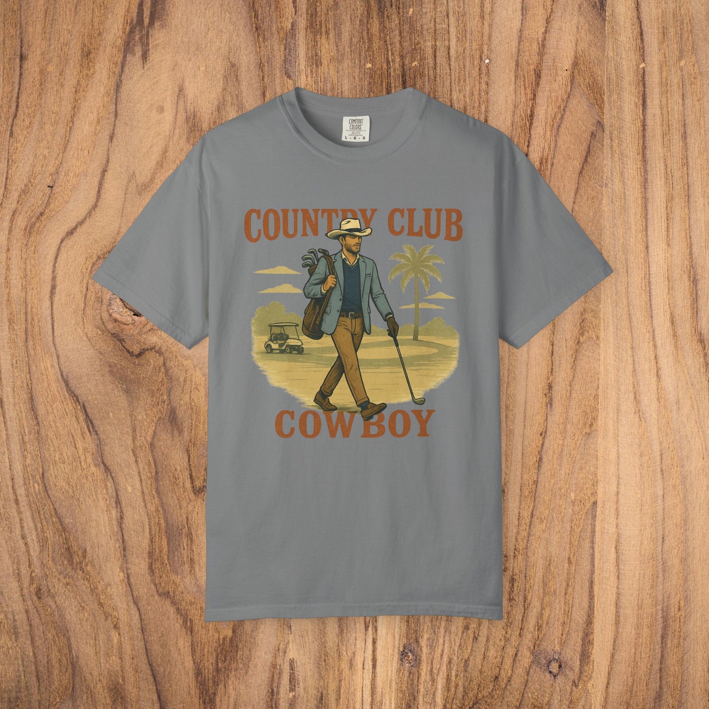 Country Club Cowboy Graphic Tee in gray, depicting a cowboy walking with golf clubs in a serene landscape. This durable cotton tee features a ribbed collar for lasting quality.