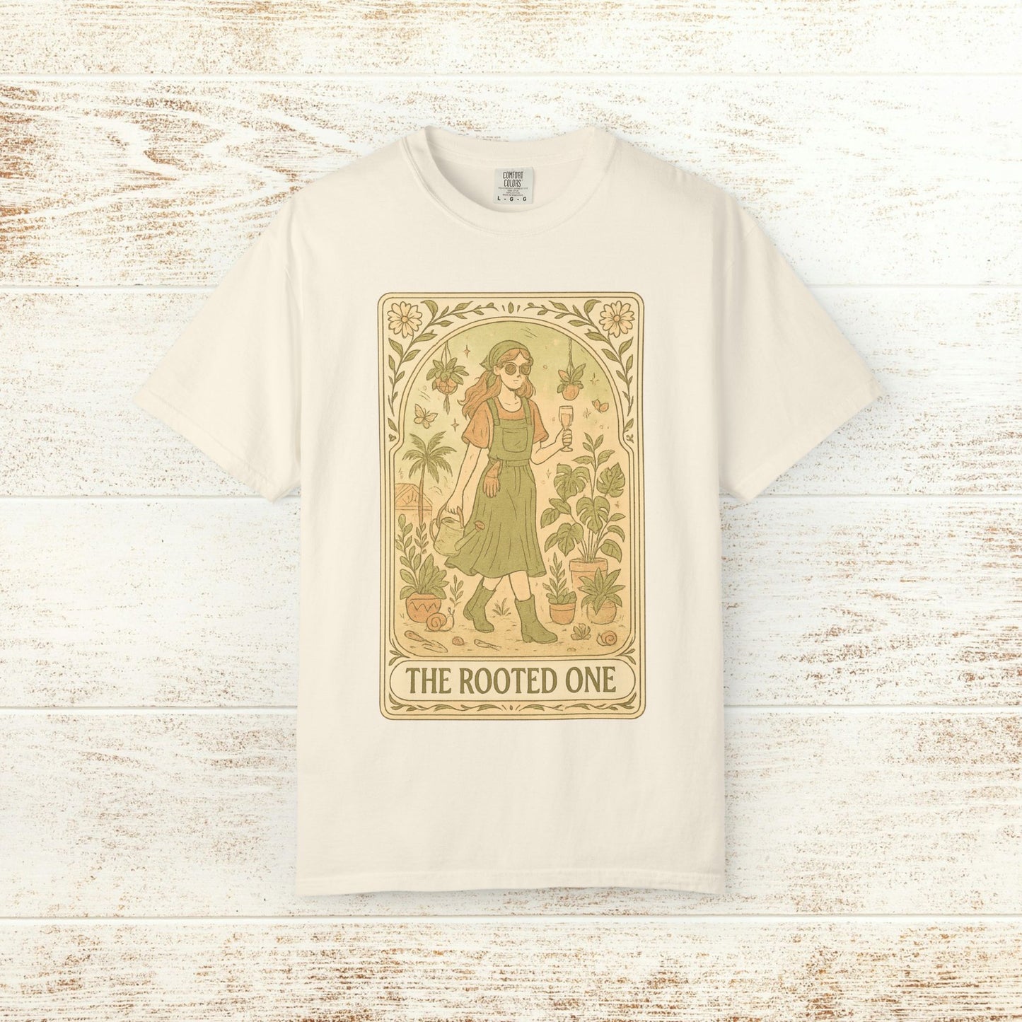 Rooted One Tarot Tee in natural beige, displaying a whimsical illustration of a figure surrounded by flora. Crafted from high-quality, ethically sourced cotton.