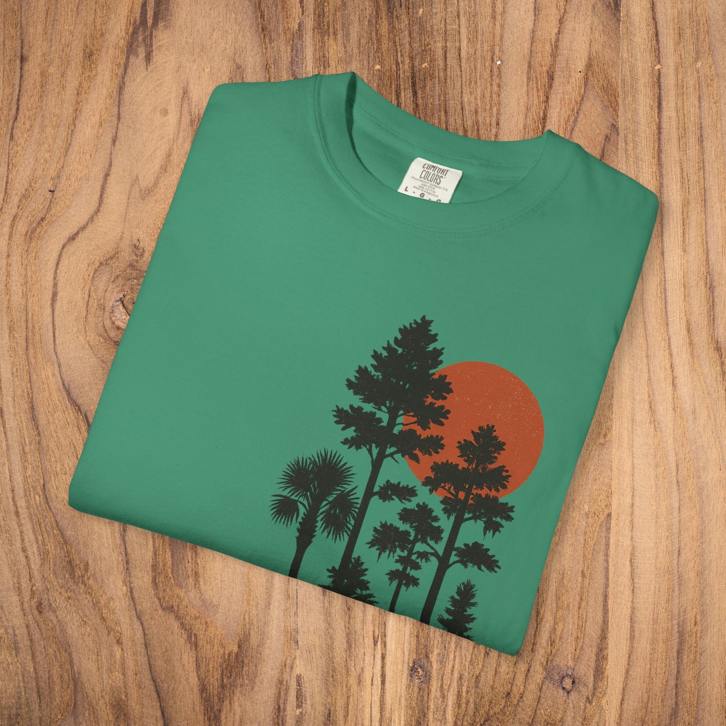 Front laid flat view of the Sunset Trees Unisex T-Shirt featuring a striking sunset design on a green background, made from high-quality 100% cotton.