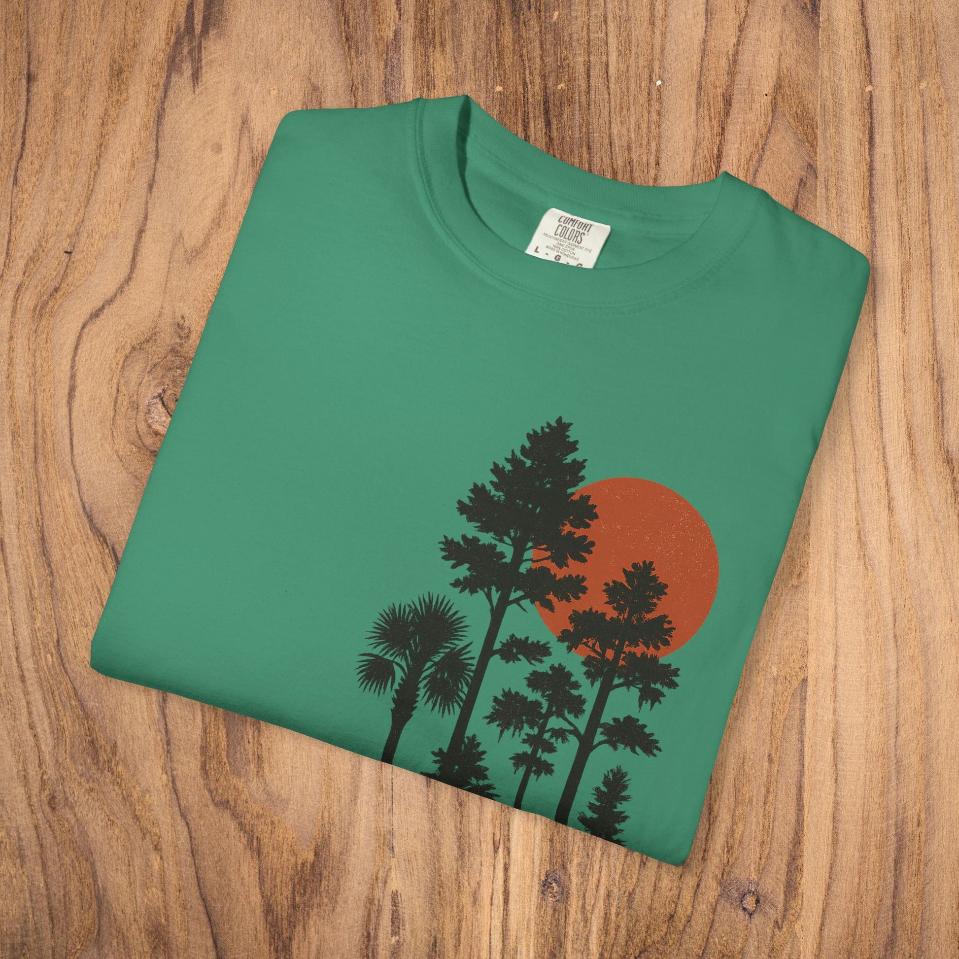 Front laid flat view of the Sunset Trees Unisex T-Shirt featuring a striking sunset design on a green background, made from high-quality 100% cotton.