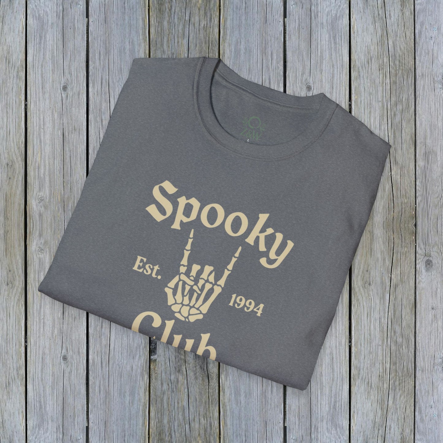 Folded Unisex Spooky Club Tee in heather gray, resting on a rustic wooden surface. The tee features a skeleton hand and 'Spooky Club Est. 1994' text, made from soft 100% cotton for a comfy Halloween wear.
