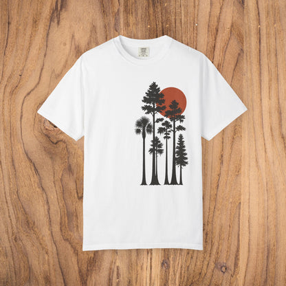 Sunset Trees Unisex T-Shirt in classic white, made from soft 100% cotton with a unique garment-dyed finish, presented against a natural wooden backdrop.
