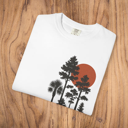 Folded white Sunset Trees Unisex T-Shirt displayed on wooden background, made from 100% cotton and featuring a stunning sunset design.