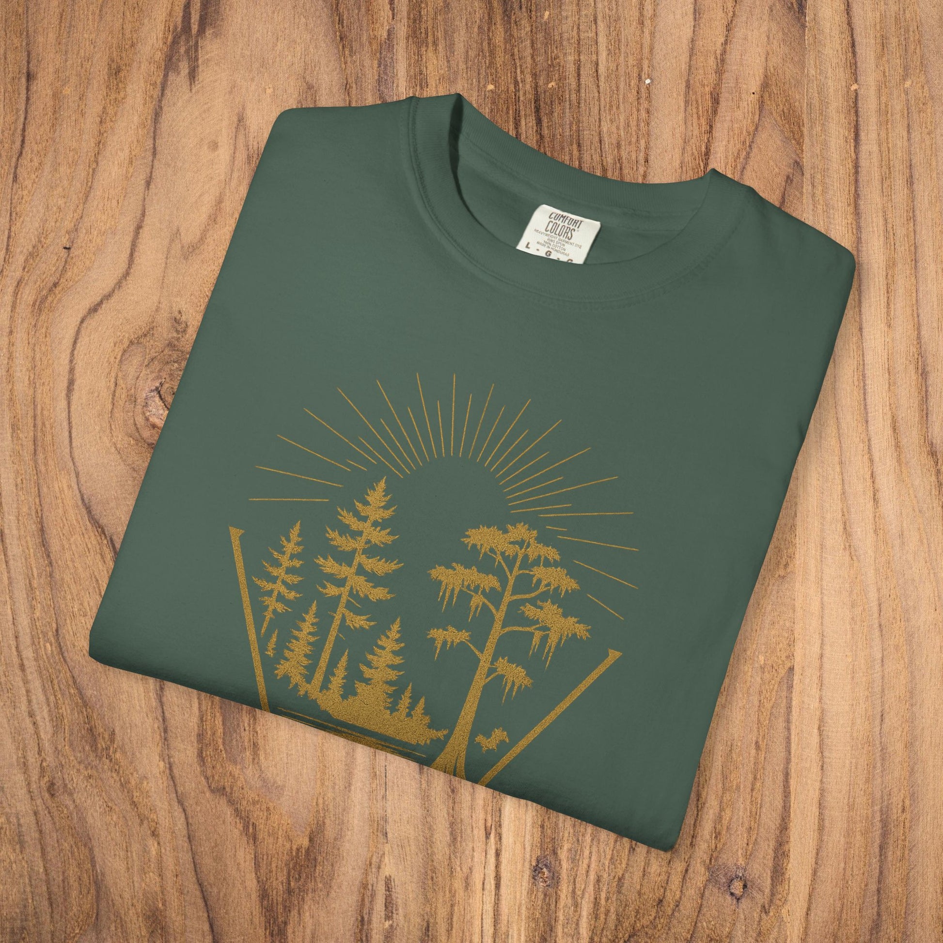 Folded Nature Outdoor Vibes Tee in forest green, displaying intricate tree graphic with sun rays, made from durable and soft 100% US cotton. Perfect for outdoor enthusiasts.