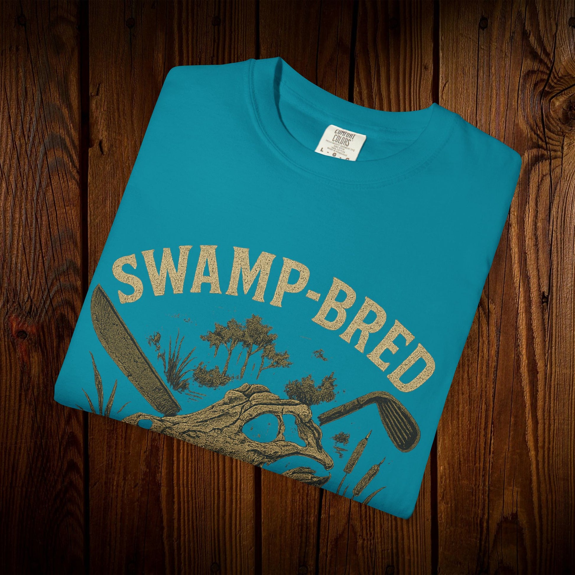 Unisex Swamp-Bred Fairway-Fed Tee displayed in vibrant turquoise with an eye-catching print, crafted from 100% pre-shrunk US cotton for ultimate comfort.