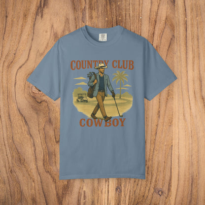 Country Club Cowboy Graphic Tee in slate blue featuring a cowboy with a golf bag set in a scenic palm tree landscape, constructed from durable cotton, equipped with ribbed collar and eco-conscious crewneck.