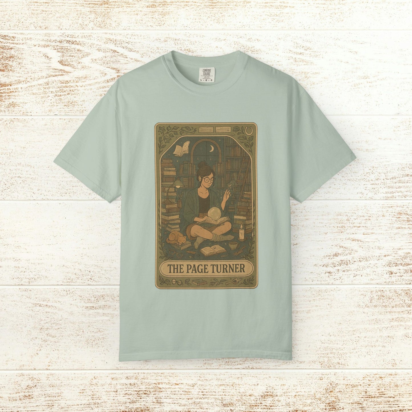 Page Turner Tarot Tee in light green, depicting a charming scene of an individual reading in a book-filled space, designed for comfort and eco-friendliness, available in sizes S to 4XL.