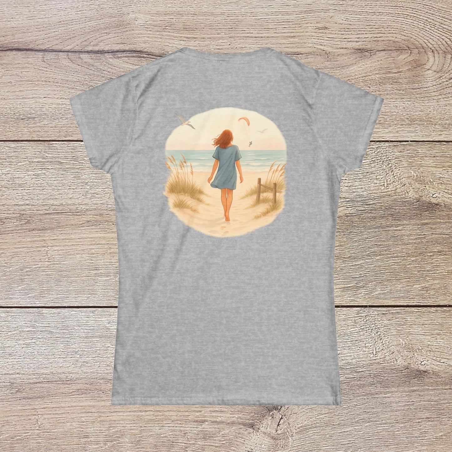 Back view of a woman walking along the beach in the Women's Coastal Spirit Midweight Cotton Tee, highlighting its relaxed and casual beachwear style.