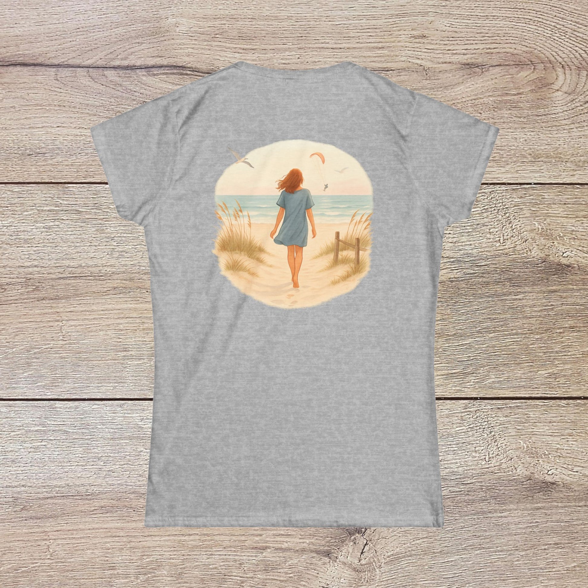 Back view of a woman walking along the beach in the Women's Coastal Spirit Midweight Cotton Tee, highlighting its relaxed and casual beachwear style.