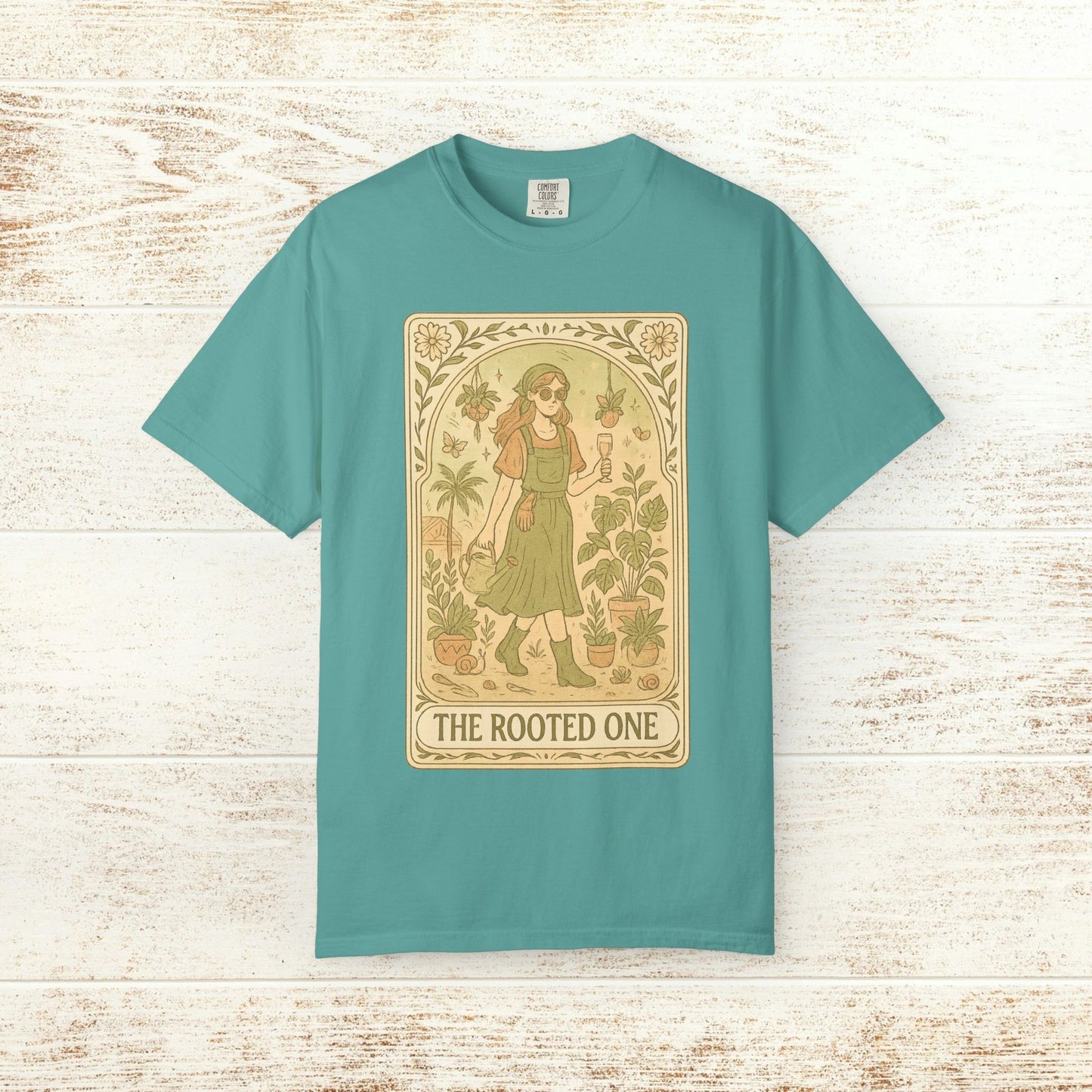 Rooted One Tarot Tee in soft seafoam green, highlighting a whimsical artwork of a woman in a botanical setting. Ethically produced cotton, available from sizes S to 4XL.