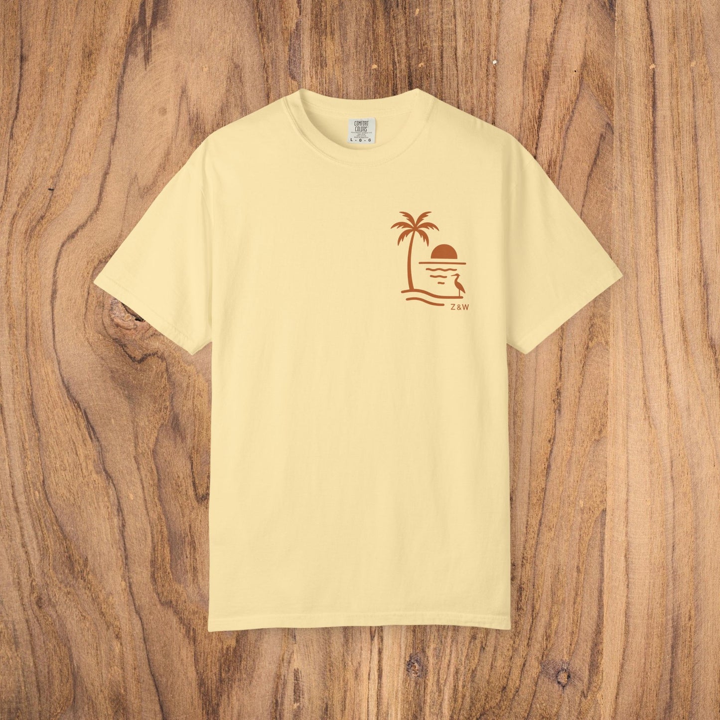Unisex Sunset Palm Tree T-Shirt in soft pastel yellow. This vibrant garment-dyed cotton tee for men and women showcases a stylish palm tree and sunset design, available in 58 colors.