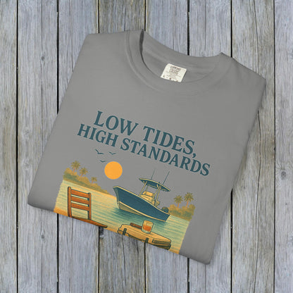 Folded Garment-Dyed Low Tides High Standards T-Shirt in gray, featuring a boat and sunny beach scene in the design. Perfect for beach outings or casual hangouts.