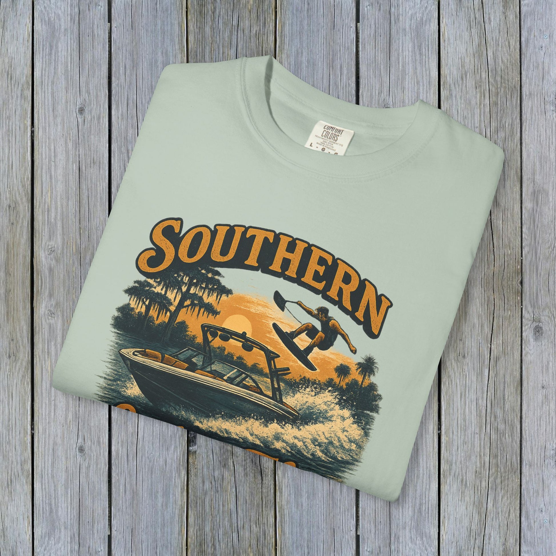 Flat lay of Southern Lake Flow T-Shirt in a soft green color, crafted from 100% US cotton, highlighting sustainable fashion with a vintage boat graphic.