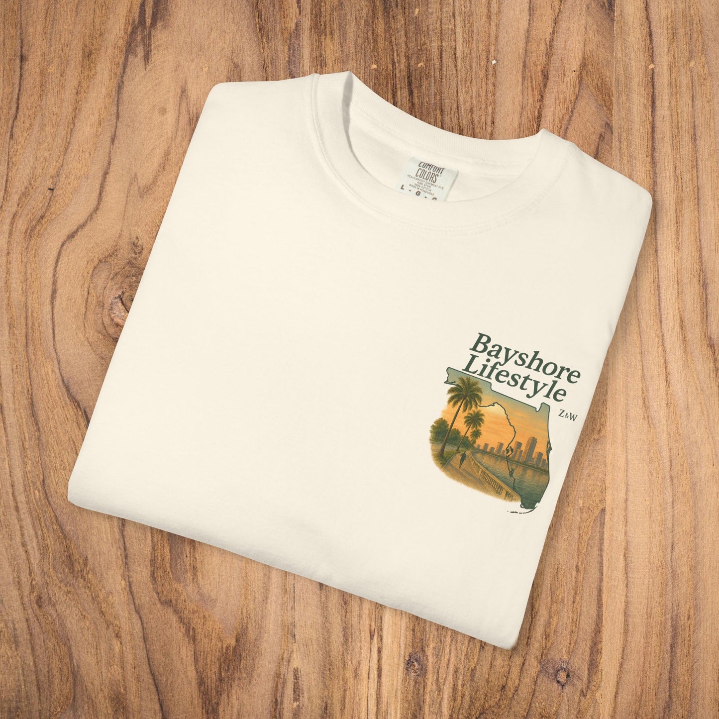 Bayshore Lifestyle Tee - Folded white t-shirt featuring a graphic design, laid out on a wooden surface.