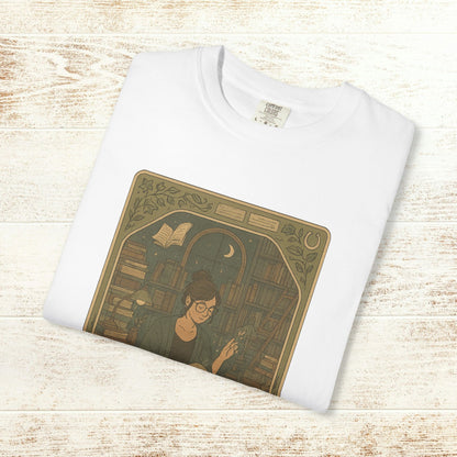Page Turner Tarot Tee in white, highlighting a charming illustration of a bookish woman in a library setting, crafted from comfortable, eco-friendly cotton.
