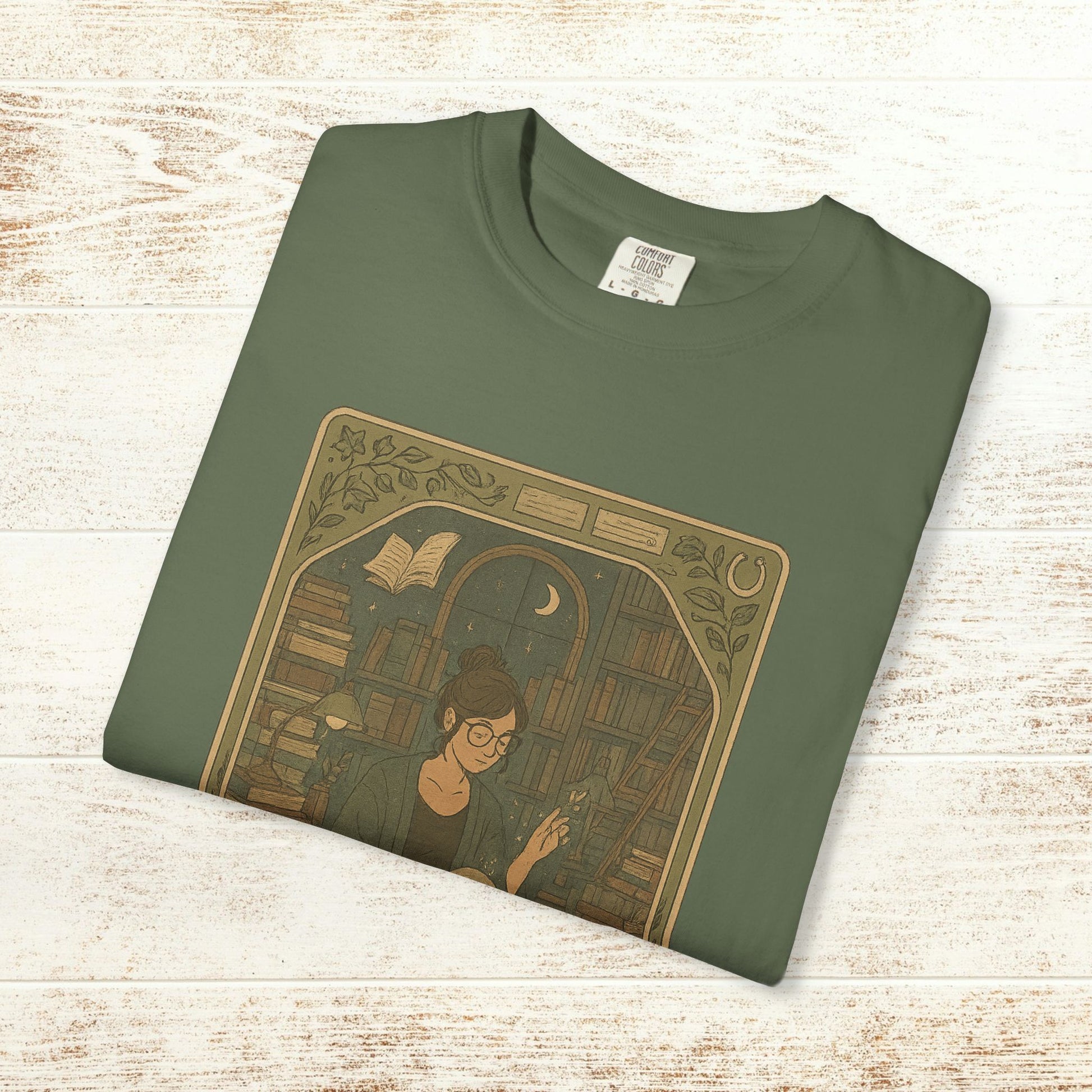 Page Turner Tarot Tee in olive green, featuring an illustration of a woman with glasses surrounded by books, showcasing a mystical theme and eco-friendly cotton fabric.