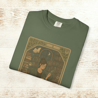 Page Turner Tarot Tee in olive green, featuring an illustration of a woman with glasses surrounded by books, showcasing a mystical theme and eco-friendly cotton fabric.
